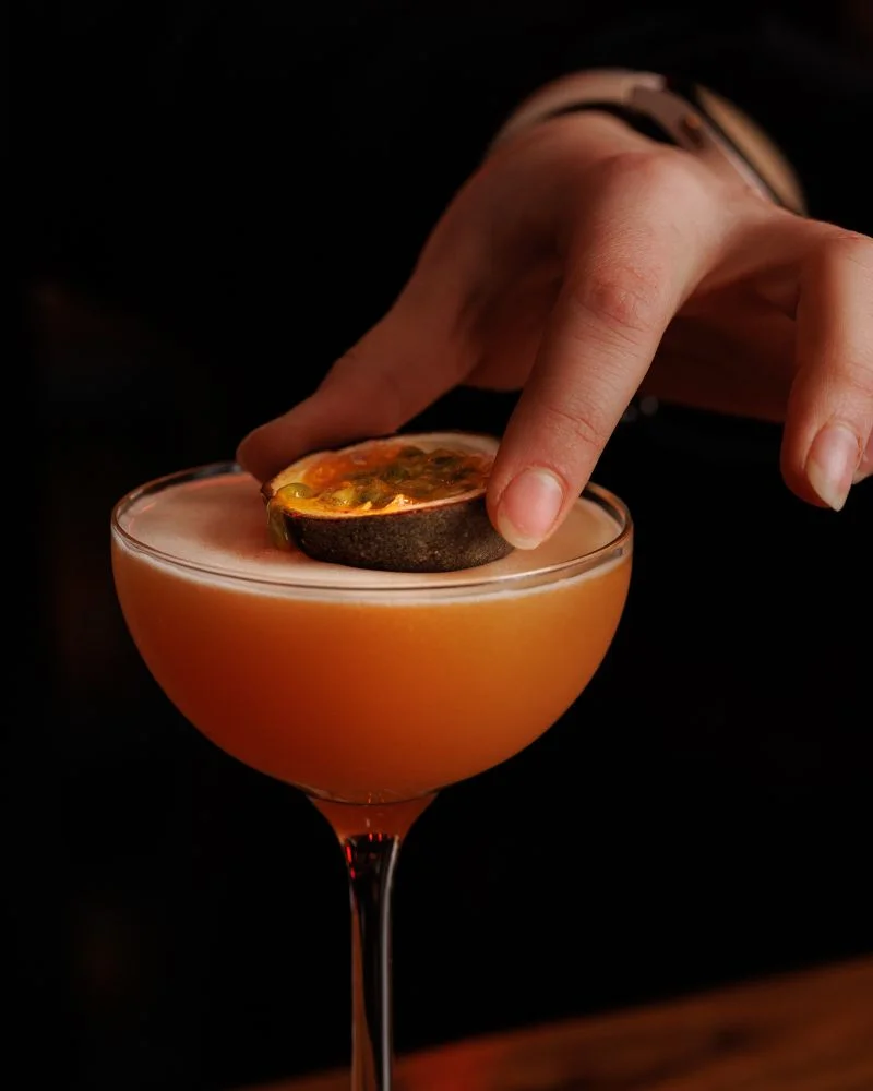 A bartender carefully garnishes a cocktail with a citrus twist, showcasing a garnishing technique in a Dublin cocktail making class.
