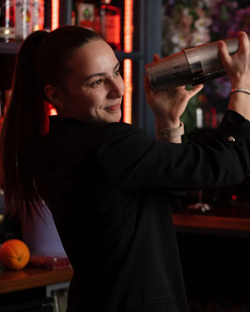 A mixologist shakes a cocktail shaker with expertise and a smile, demonstrating during a cocktail making class in Dublin.