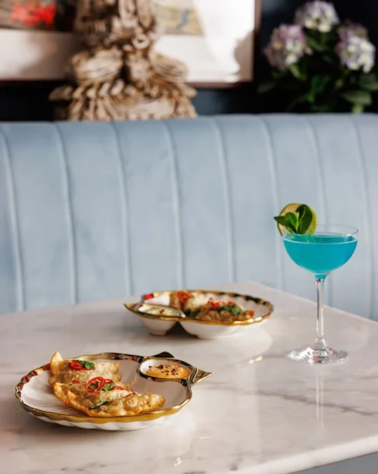 Elegant plating of dumplings paired with a vibrant blue cocktail on a marble table, showcasing Temple Bar's dining experience.