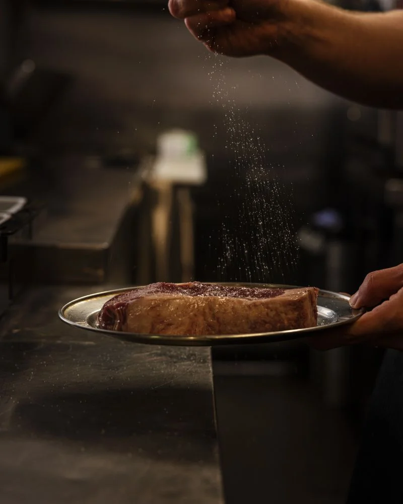 A chef's hands meticulously seasoning a steak, a glimpse into the gourmet cooking techniques at a Temple Bar restaurant.