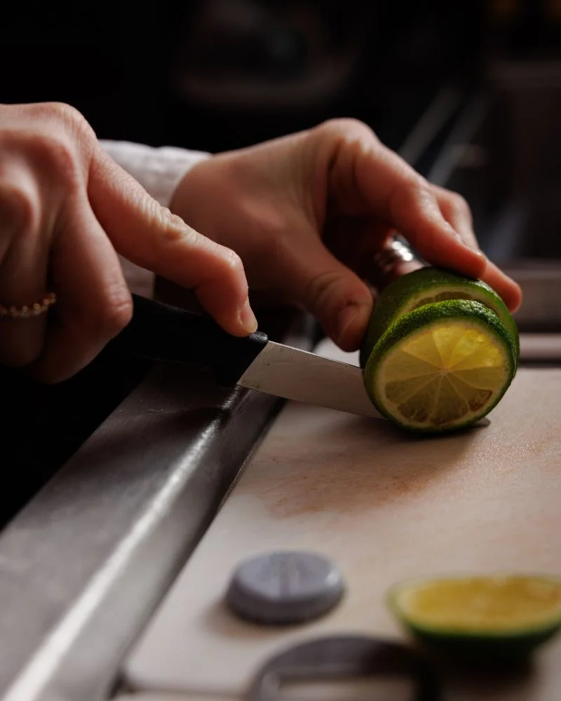 A bartender carefully slices a lime for garnishing cocktails, capturing the fresh ingredient preparation at a Temple Bar restaurant.