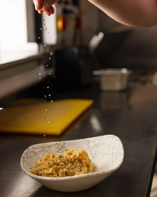 Chef sprinkling seasoning over fried rice in a Temple Bar kitchen, highlighting the attention to flavor and detail.